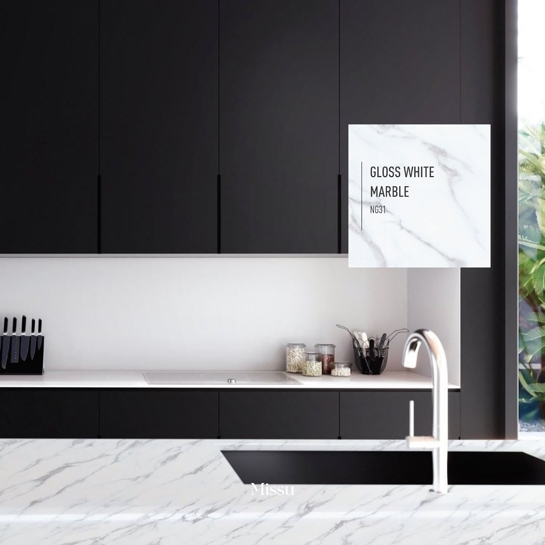 Nowoczesna kuchnia z czarnymi szafkami i blatem z białego marmuru z widocznym zlewozmywakiem i baterią oraz naklejką z informacją o rodzaju marmuru.