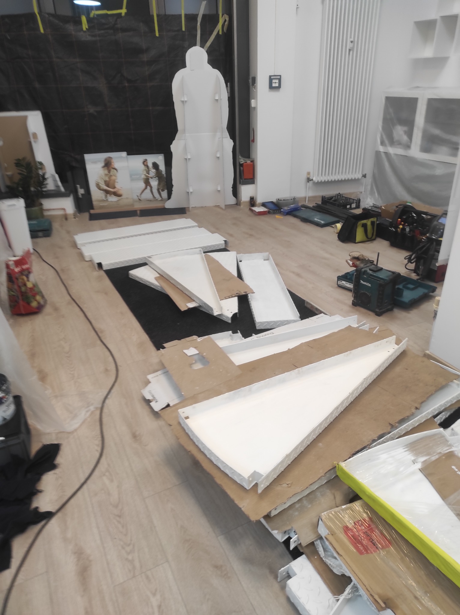 Elementy konstrukcyjne schodów metalowych, przygotowane do montażu, leżące na podłodze w pomieszczeniu z narzędziami i materiałami budowlanymi.