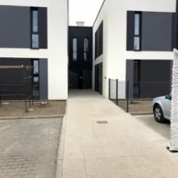 Nowoczesny budynek dwukondygnacyjny z oknami PCV w kolorze antracytowym, częściowo w trakcie wykończenia, widoczne rusztowanie i teren wokół budynku w trakcie zagospodarowywania.