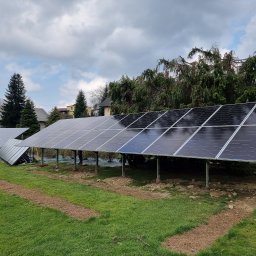 Firma Handlowo-Usługowa Patryk Szostak - Instalacja paneli słonecznych na konstrukcji wsporczej w ogrodzie, widoczne przygotowane podłoże i częściowo pochmurne niebo.
