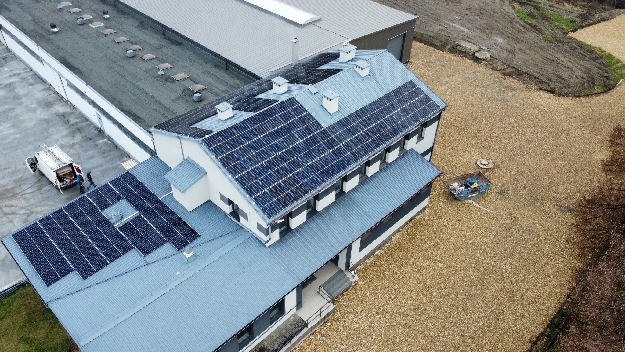 Widok z góry na budynek z panelami słonecznymi na dachu, obok stoi samochód serwisowy z otwartymi drzwiami.
