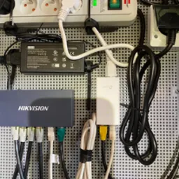 Panel krosowniczy z urządzeniami sieciowymi Hikvision i TP-Link, zasilaczem, listwą zasilającą Brennenstuhl oraz okablowaniem Ethernet, wszystko zamontowane na perforowanej płycie montażowej.
