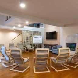 Ośrodek Terapii Uzależnień Poznaj Siebie - Jasne, przestronne wnętrze z krzesłami ustawionymi w okrąg, tablicą z napisem 'Program' i telewizorem na ścianie, prawdopodobnie sala do terapii grupowej.