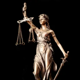 Brązowa statuetka Temidy, bogini sprawiedliwości, z wagą i mieczem na czarnym tle.