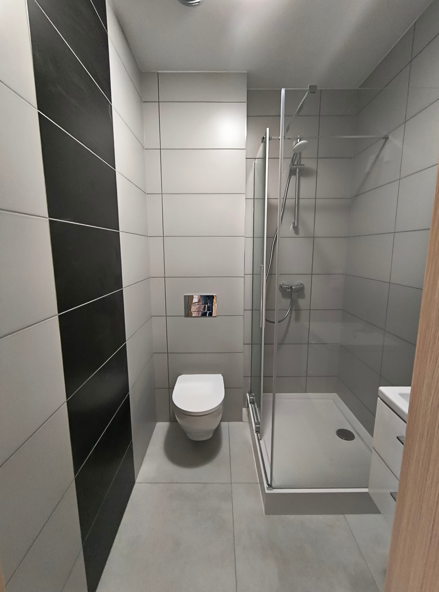 Nowoczesna łazienka z kabiną prysznicową typu walk-in, białą toaletą wiszącą i ścianą z czarno-białych płytek w geometryczny wzór.