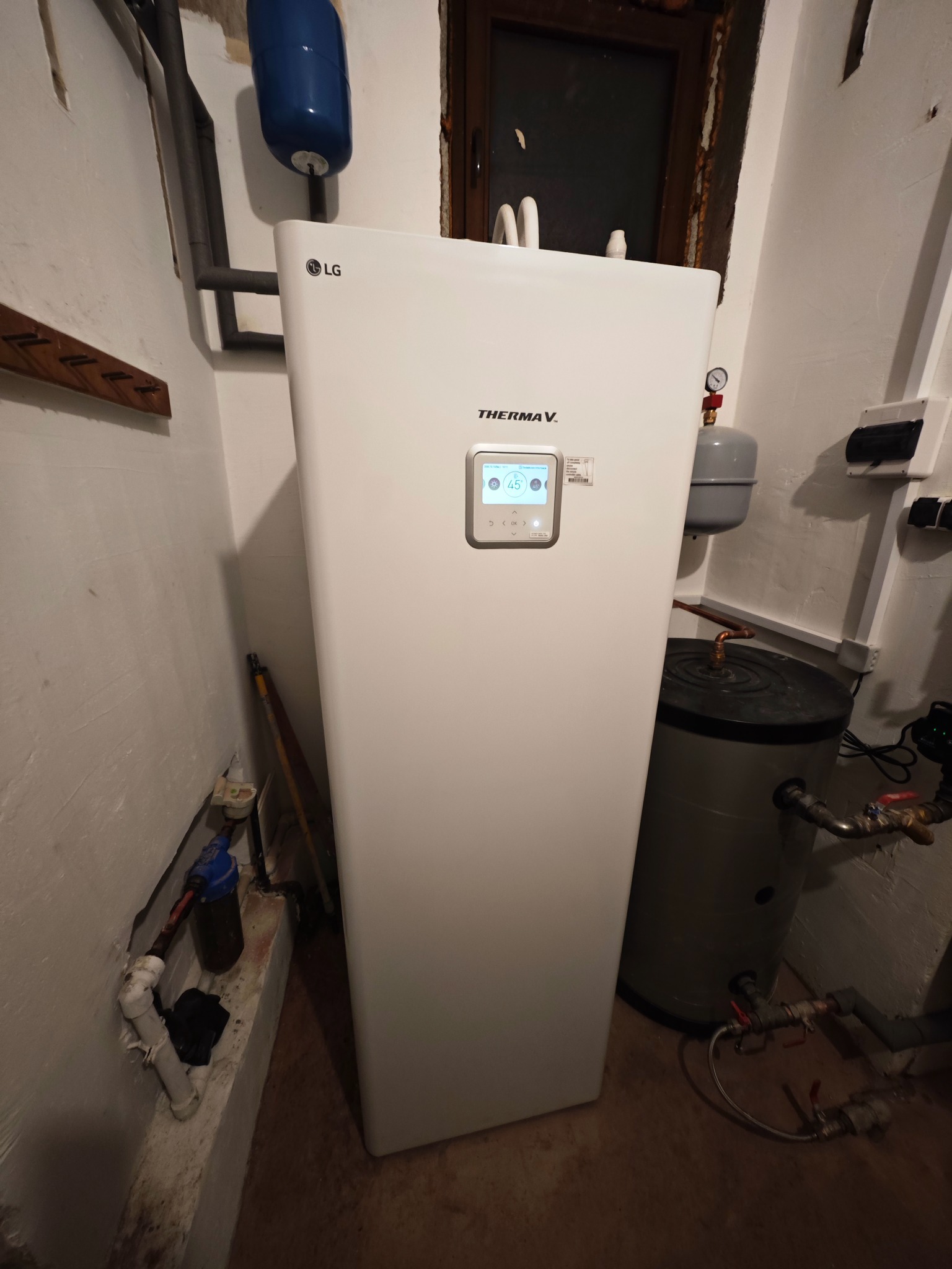 Biała pompa ciepła LG Therma V, zamontowana w kotłowni, widoczny zbiornik buforowy i instalacja hydrauliczna. Na ekranie pompy widoczna temperatura 45 stopni.