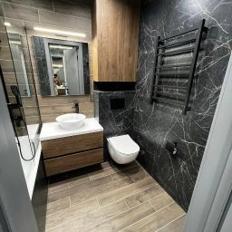 D&L remont - Nowoczesna łazienka z drewnopodobną podłogą, czarnym marmurem na ścianach, wiszącą toaletą, umywalką nablatową i grzejnikiem drabinkowym w czarnym kolorze.