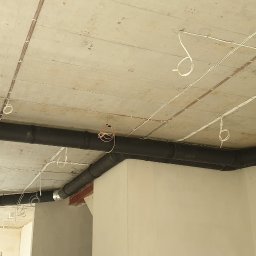 Klimbrand Adrian Kaflik - Czarny system rur wentylacyjnych pod sufitem w surowym stanie, widoczne kable elektryczne, instalacja w trakcie realizacji w Warszawie.