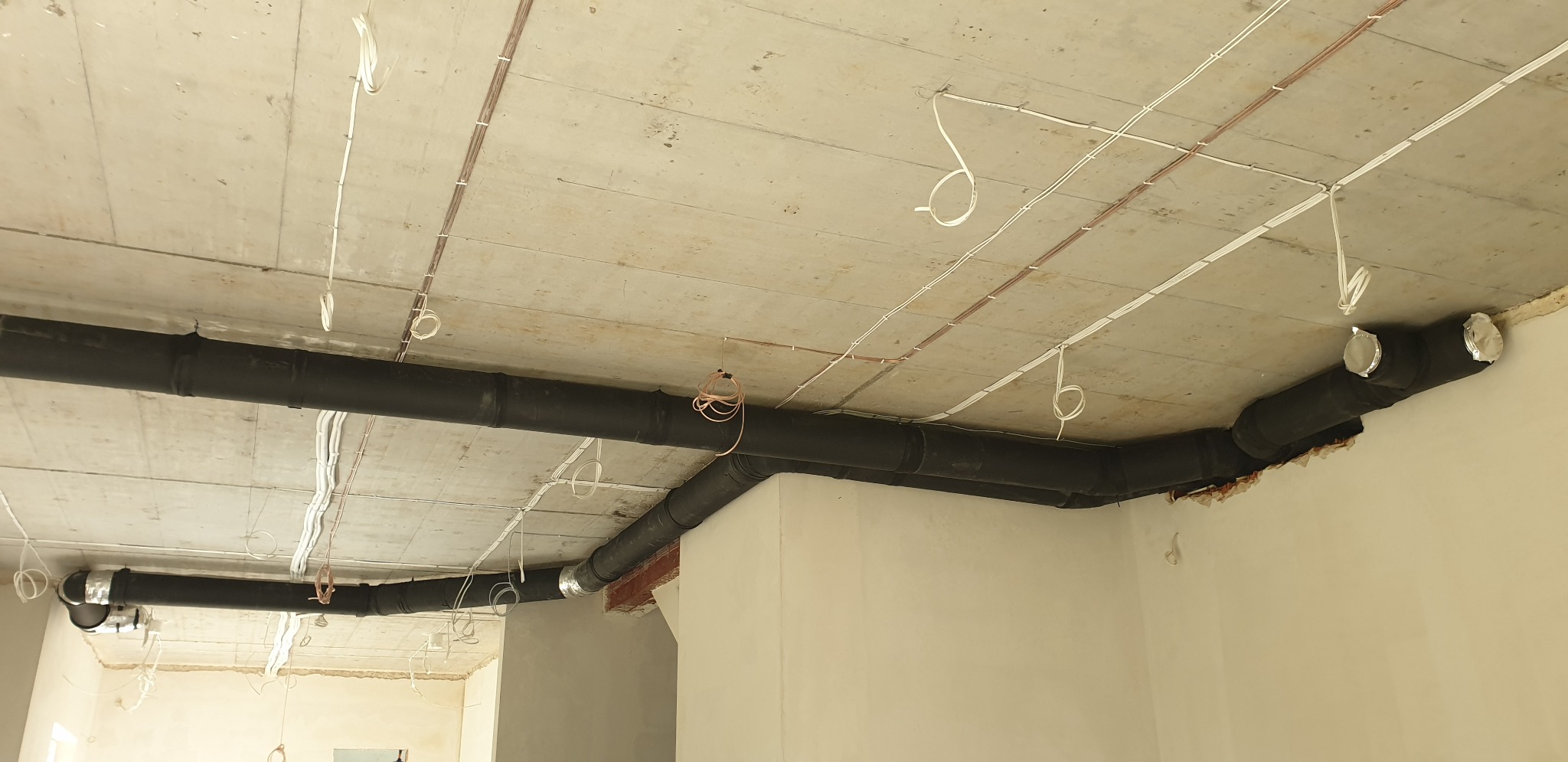 Czarny system rur wentylacyjnych pod sufitem w surowym stanie, widoczne kable elektryczne, instalacja w trakcie realizacji w Warszawie.