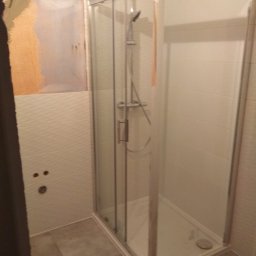 Edward Martych - Niedokończona łazienka z kabiną prysznicową z chromowanymi ramami i szklanymi drzwiami, widoczne przygotowane ściany do położenia płytek.