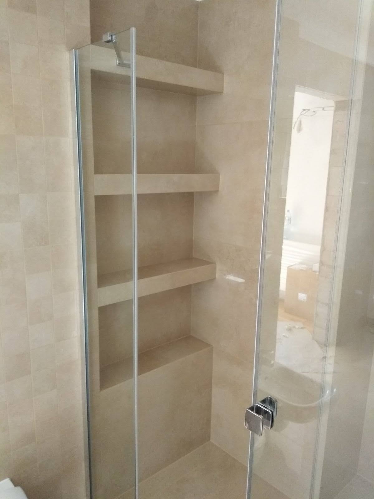 Beżowa łazienka z wnęką z półkami wyłożoną płytkami, kabina prysznicowa ze srebrnymi okuciami.