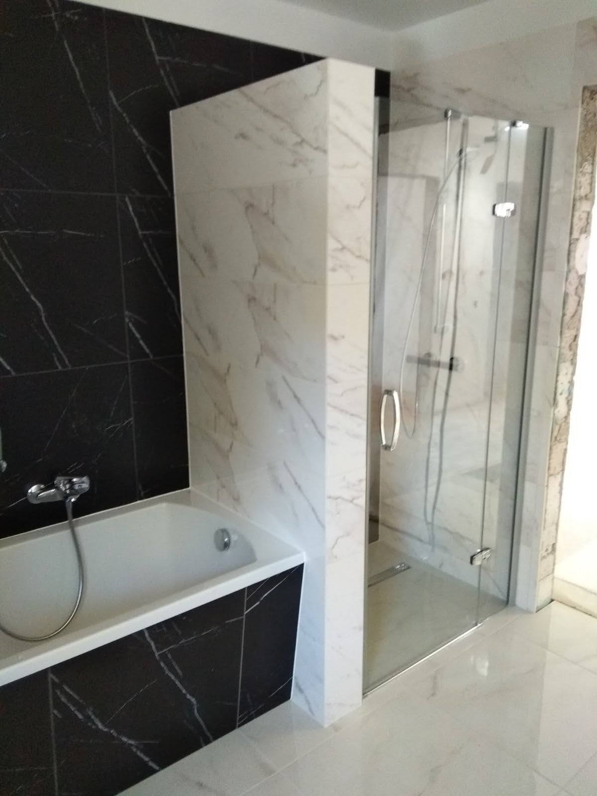 Nowoczesna łazienka z czarno-białymi płytkami imitującymi marmur, białą wanną i szklaną kabiną prysznicową z chromowanymi detalami.