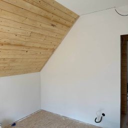 Ruslan Sidletskyi Group - Poddasze z drewnianą boazerią i pomalowanymi na biało ścianami w Kłodzku. Widoczne narzędzia i surowa podłoga, sugerujące etap wykończeniowy.