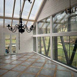 Ruslan Sidletskyi Group - Jasne wnętrze z dużymi oknami i przeszklonym dachem, wykończone drewnem i szarą podłogą w kratkę. Dwa czarne żyrandole dodają elegancji.