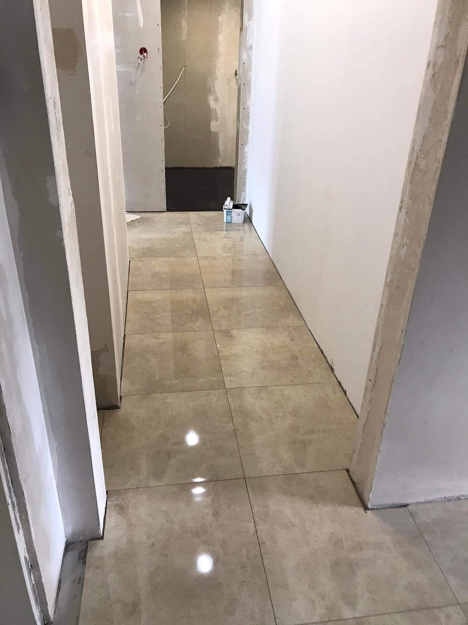 Wnętrze w trakcie remontu w Bydgoszczy: ułożone beżowe płytki podłogowe, ściany w trakcie przygotowania do malowania, widoczne płyty kartonowo-gipsowe i pojemnik z masą szpachlową w tle.