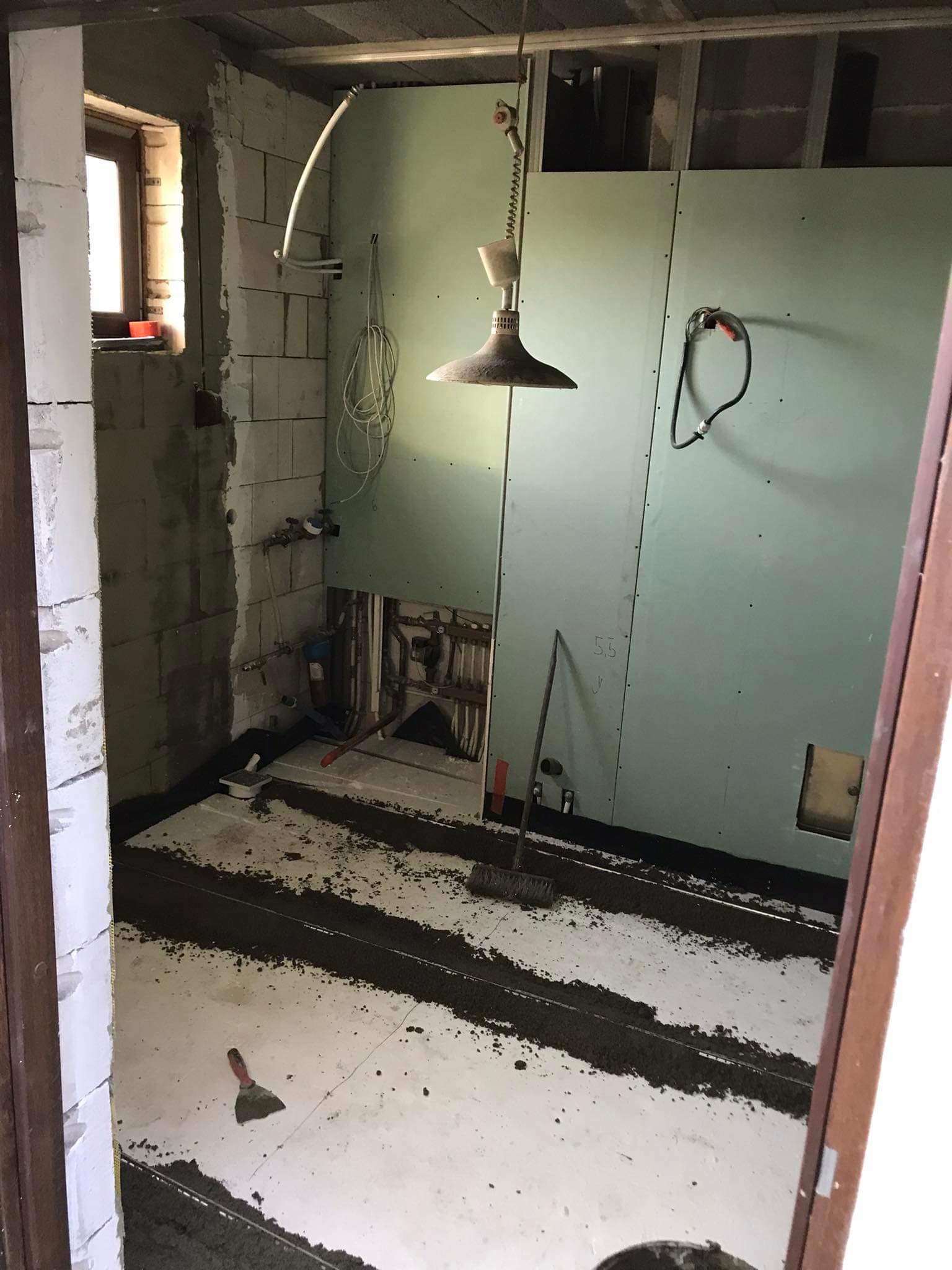 Remont łazienki w trakcie: ściany z płyty karton gips, przygotowanie podłoża pod płytki, widoczne instalacje hydrauliczne i prowizoryczne oświetlenie.