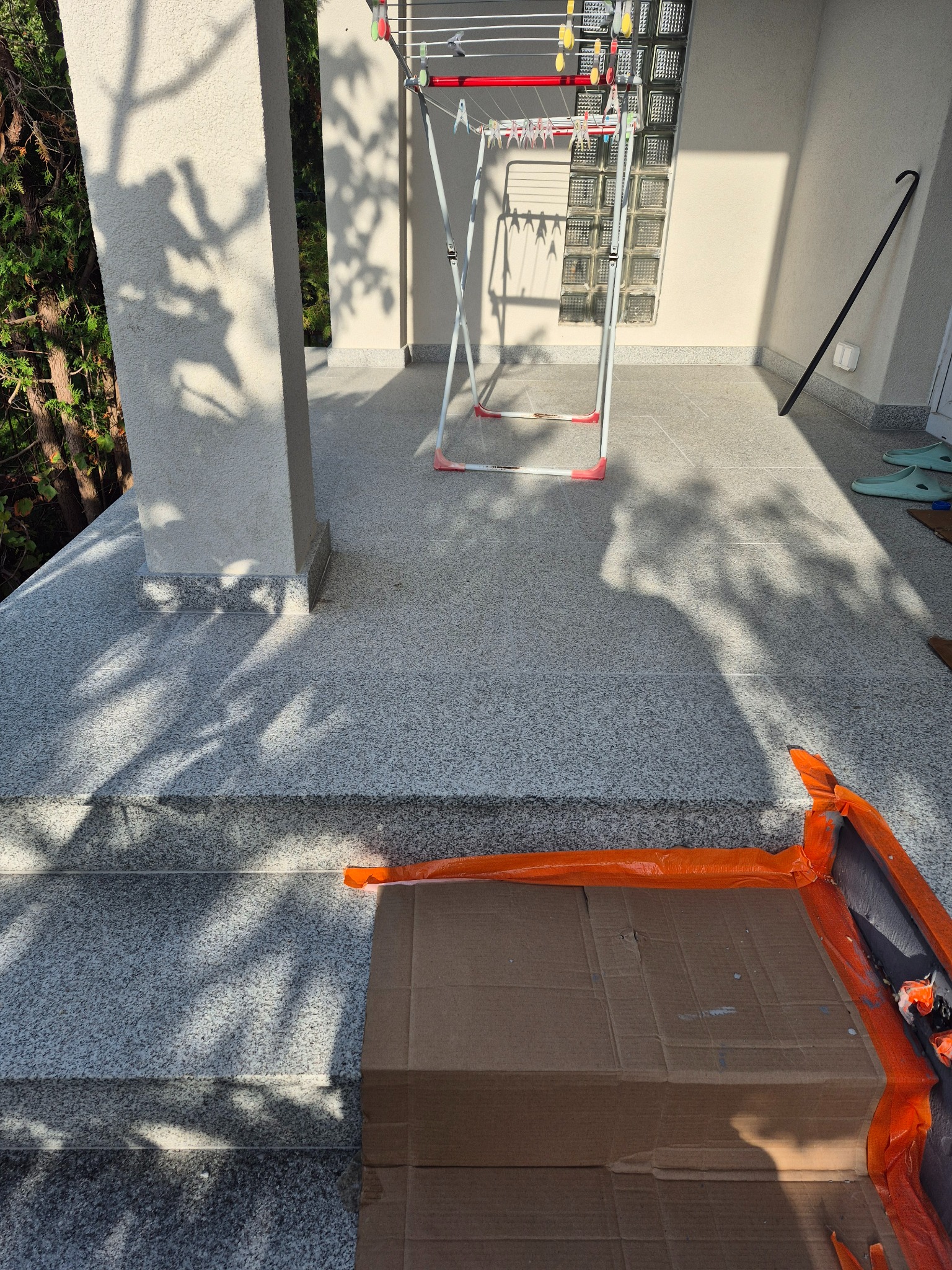 Jasny, wykafelkowany taras z widocznymi schodami i przygotowanym kartonem z folią ochronną, sugerujący prace wykończeniowe na zewnątrz.