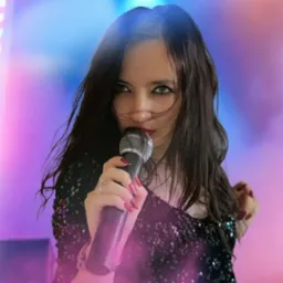 Ujęcie wokalistki z mikrofonem na tle sceny z efektami świetlnymi. Ciemne włosy, błyszcząca sukienka, czerwone usta. Koncert w blasku reflektorów.