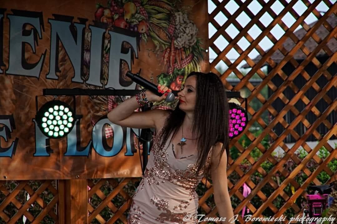 Kobieta w sukience z cekinami śpiewa do mikrofonu na scenie z oświetleniem punktowym.