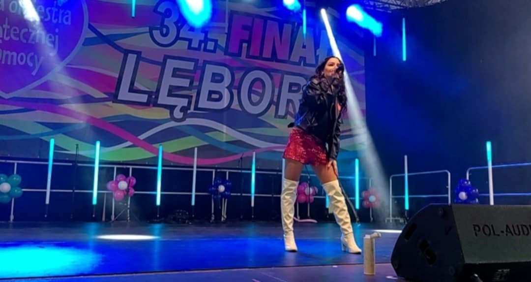 Wokalistka w błyszczącej sukience i kozakach na scenie podczas koncertu, oświetlona niebieskim światłem, z widocznym logo Pol-Audio na głośniku.