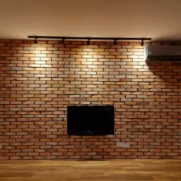 Ściana z cegły klinkierowej w salonie z zamontowanym telewizorem i klimatyzatorem, oświetlona reflektorami szynowymi, parkiet na podłodze.