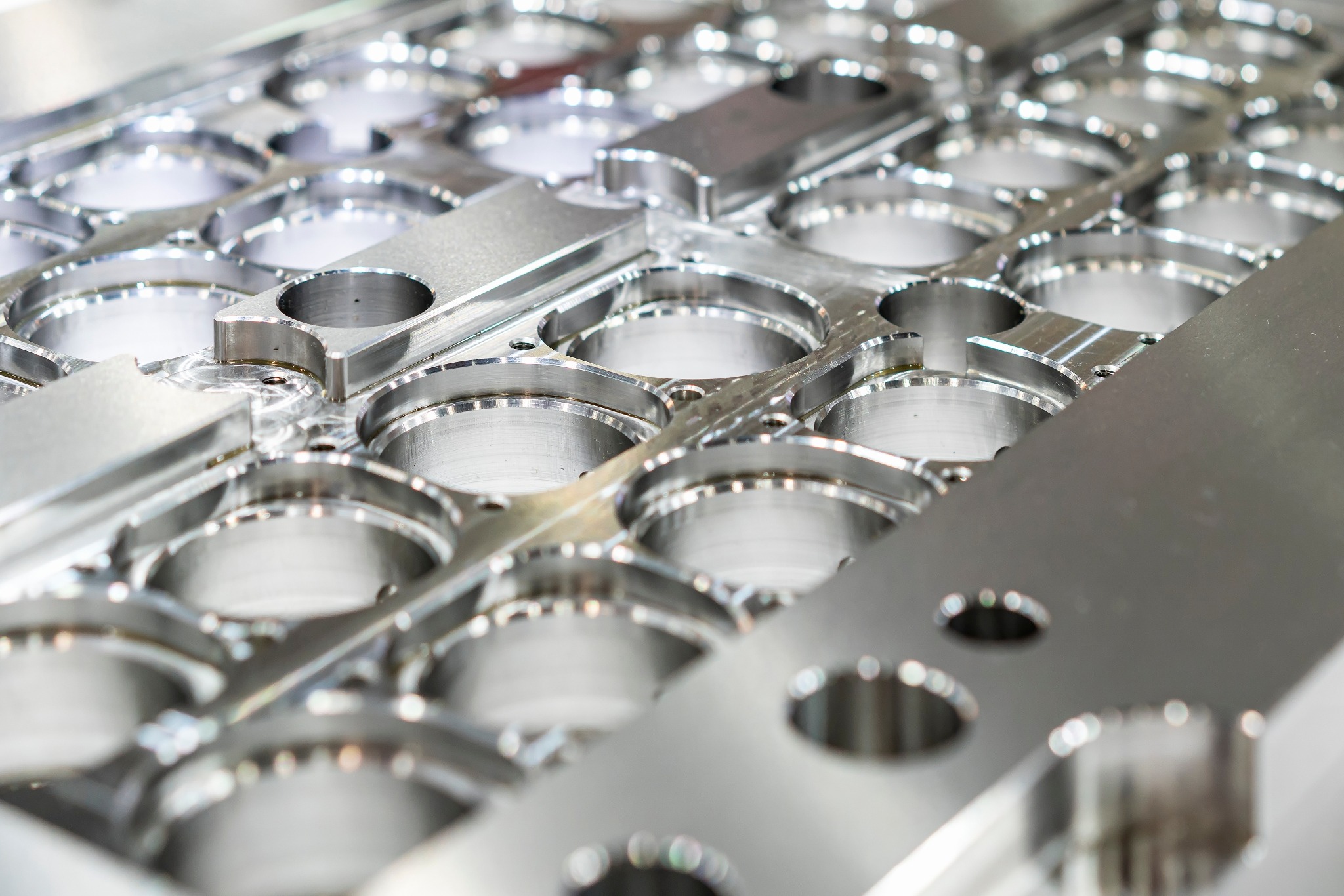 Metalowa forma z licznymi okrągłymi otworami i elementami łączącymi, wykonana z polerowanego aluminium, widoczna z bliska pod kątem, ukazująca precyzję obróbki.