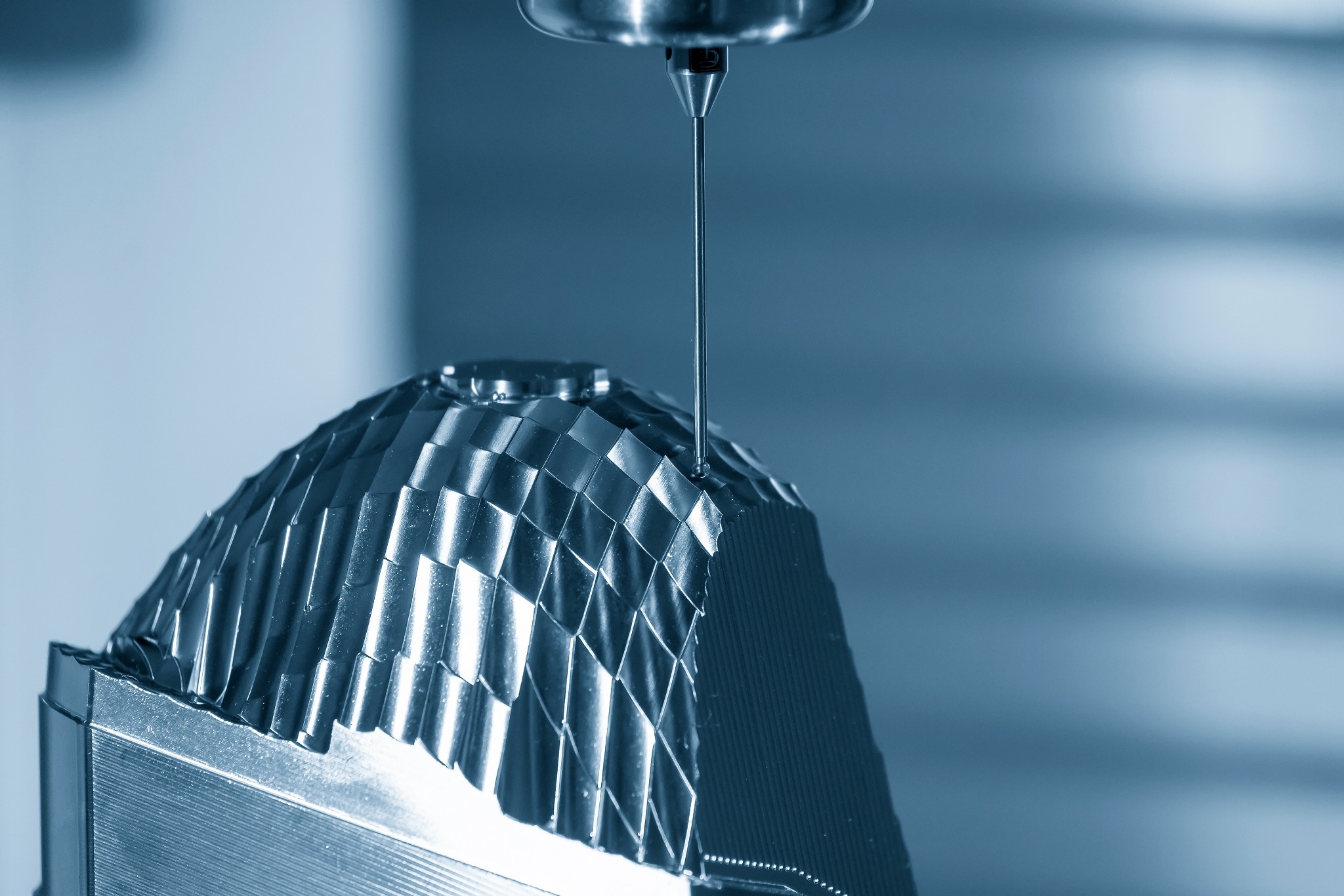 Precyzyjny pomiar geometryczny skomplikowanego elementu o powierzchni fasetowanej, wykonywany za pomocą sondy pomiarowej na maszynie współrzędnościowej CMM w chłodnym, niebieskawym oświetleniu.