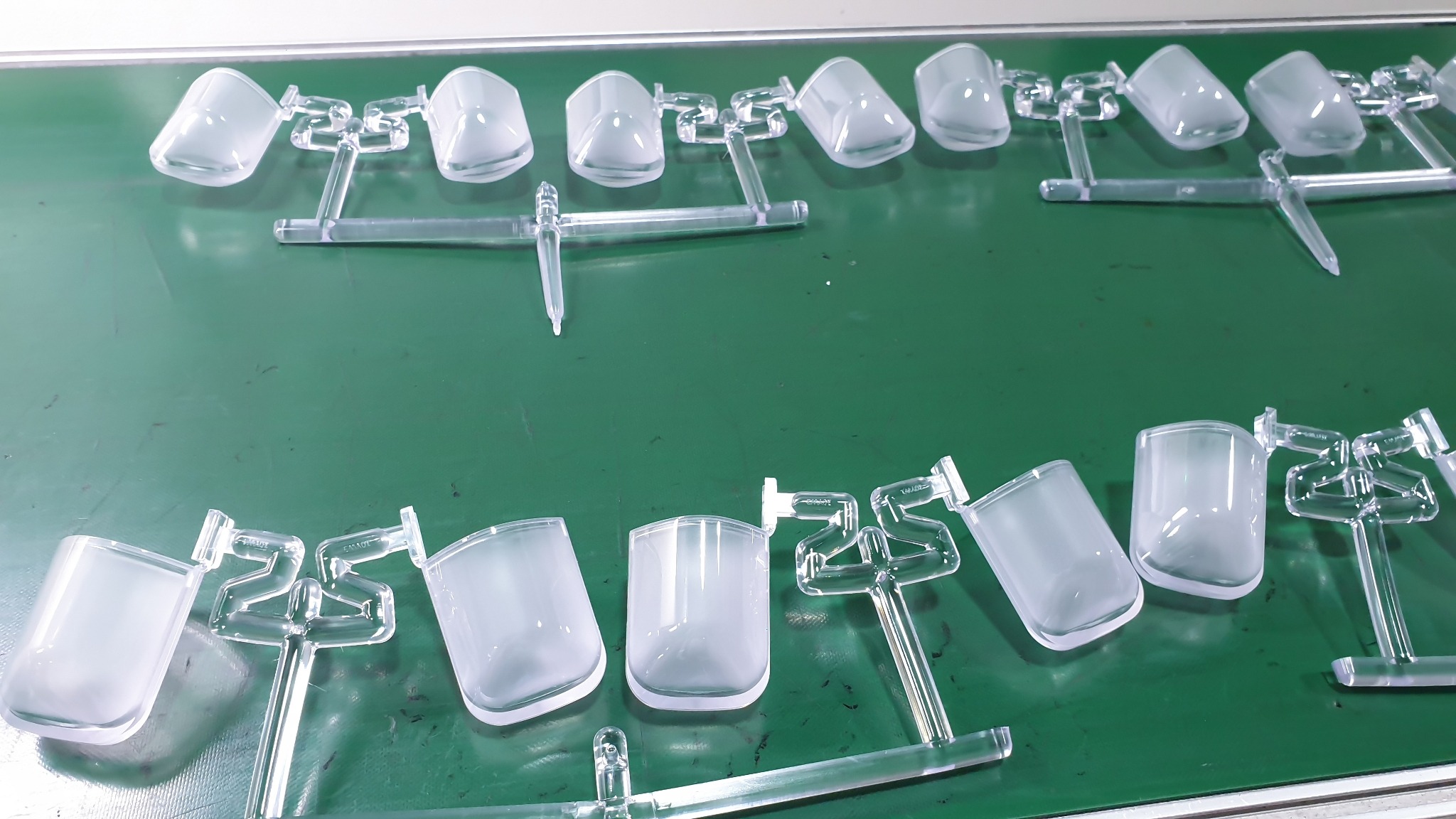 Formowane, przezroczyste plastikowe elementy opakowań na zielonym tle, połączone cienkimi łącznikami, tworzące arkusz z wieloma sztukami.