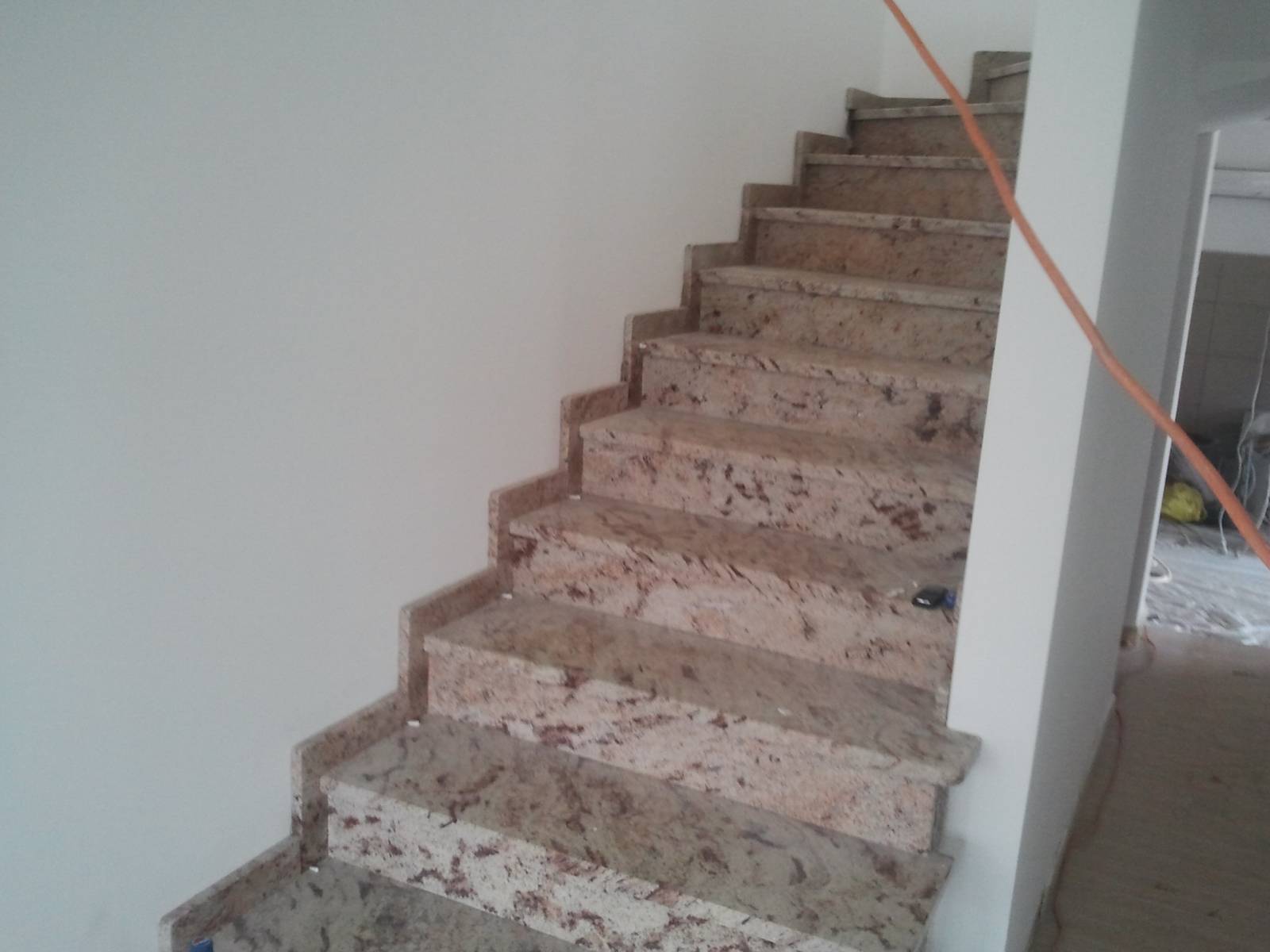 Wykończone schody kamienne z brązowo-beżowego granitu w Goleniowie, widoczne z dołu do góry, z pomarańczowym kablem w tle i śladami prac wykończeniowych w pomieszczeniu.