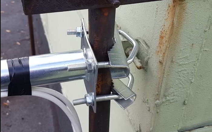 Mocowanie anteny satelitarnej do metalowej konstrukcji za pomocą śrub i uchwytów, widoczne kable zabezpieczone czarną taśmą izolacyjną.