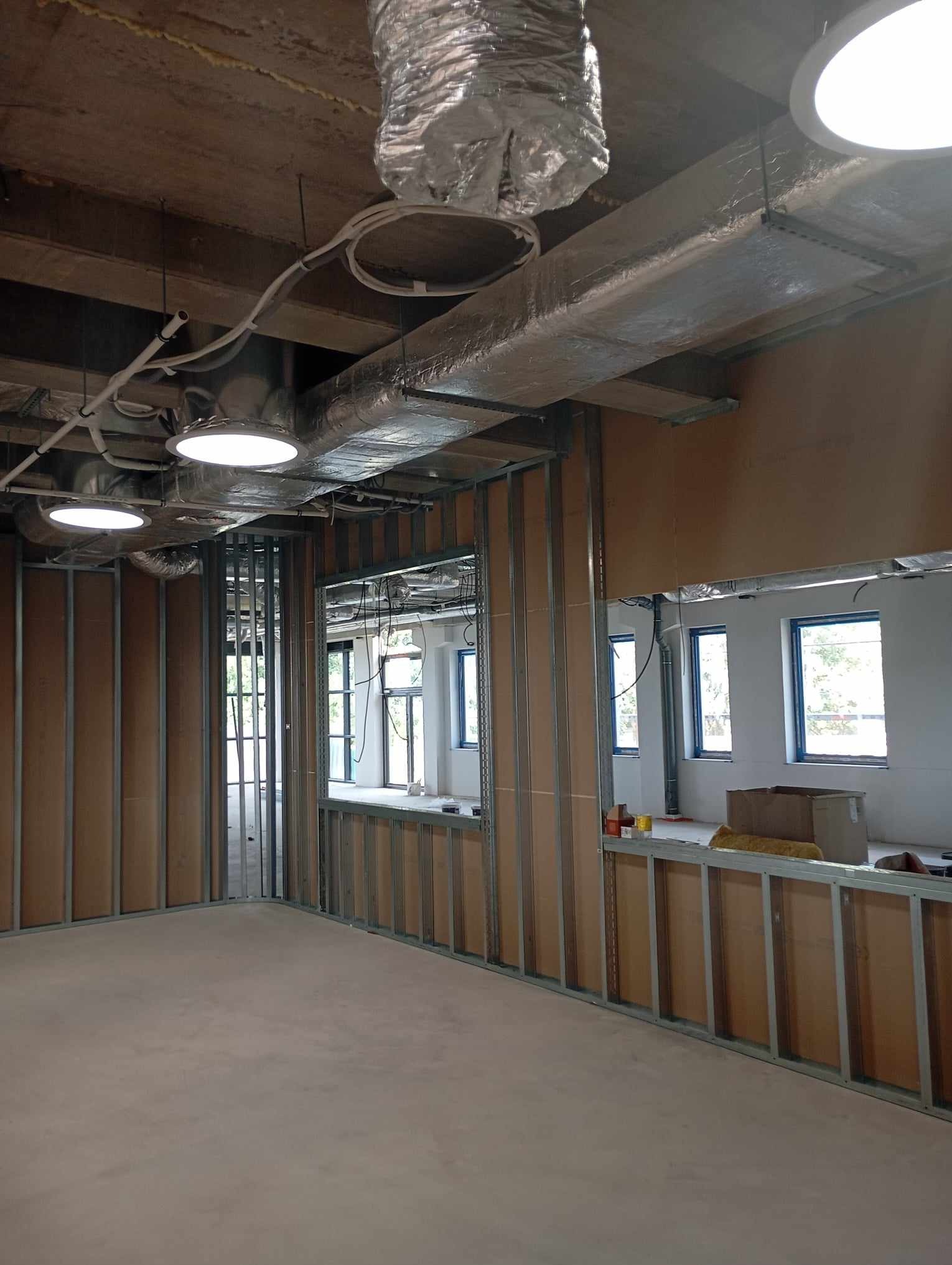 Wnętrze w trakcie montażu ścian działowych z metalowych profili i płyt, widoczne instalacje pod sufitem, surowy beton na podłodze.