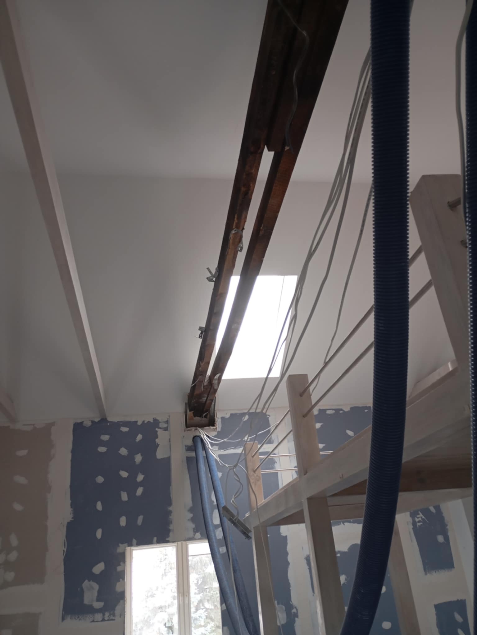 Wnętrze w trakcie remontu: ściany przygotowane pod malowanie, widoczne elementy drewniane konstrukcji sufitu, instalacja elektryczna i rury wentylacyjne.