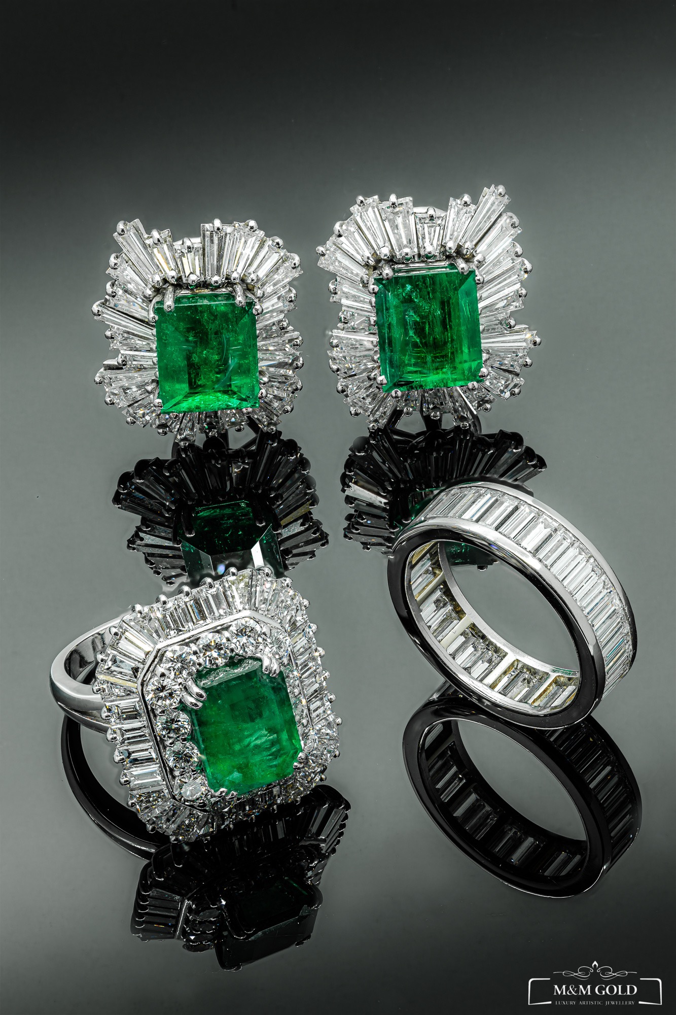 Szmaragdowe kolczyki i pierścionki z brylantami na czarnym, błyszczącym tle, tworzące symetryczne odbicie.