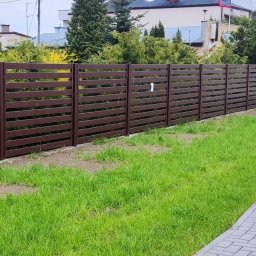 KWK SPAW mobilne naprawy spawalnicze - Nowoczesne, poziome ogrodzenie z ciemnobrązowych paneli drewnopodobnych, oddzielające posesję od chodnika z kostki, z widoczną skrzynką elektryczną i fragmentem zaparkowanego samochodu dostawczego...