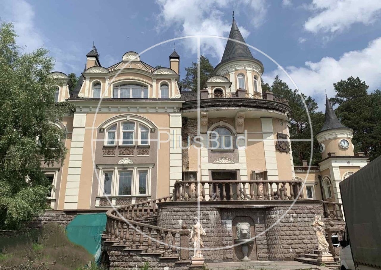 Elewacja budynku w stylu pałacowym z wieżyczkami, balkonem z kamienną balustradą i rzeźbami, widoczny fragment schodów wejściowych.