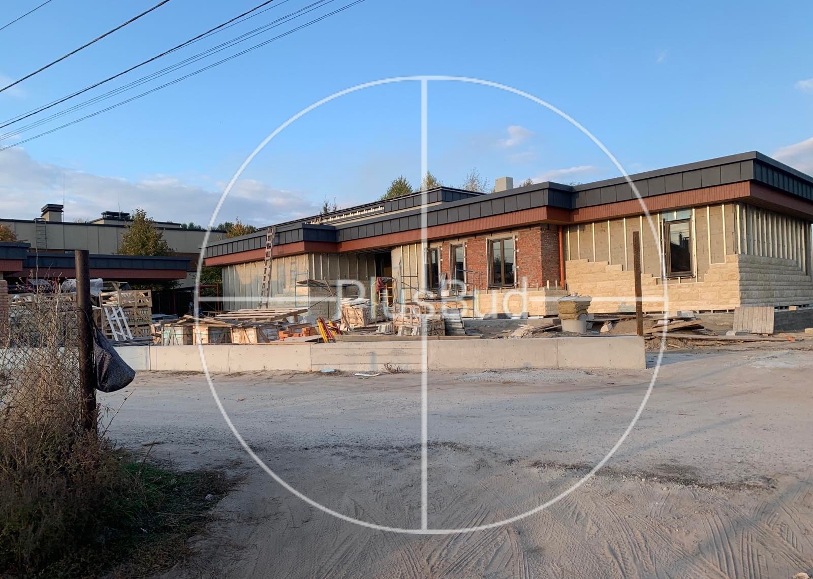 Budynek w trakcie wykańczania elewacji z kamienia i cegły, widoczne rusztowania i materiały budowlane, surowy teren.