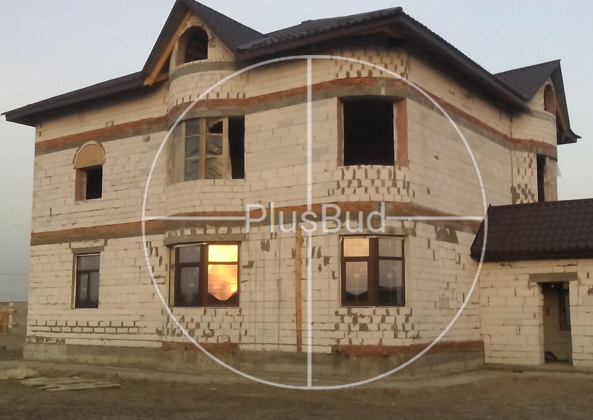 Dwupiętrowy dom w trakcie budowy z białej cegły z brązowym dachem, widoczne okna z odbijającym się słońcem, na elewacji nałożony znak wodny.