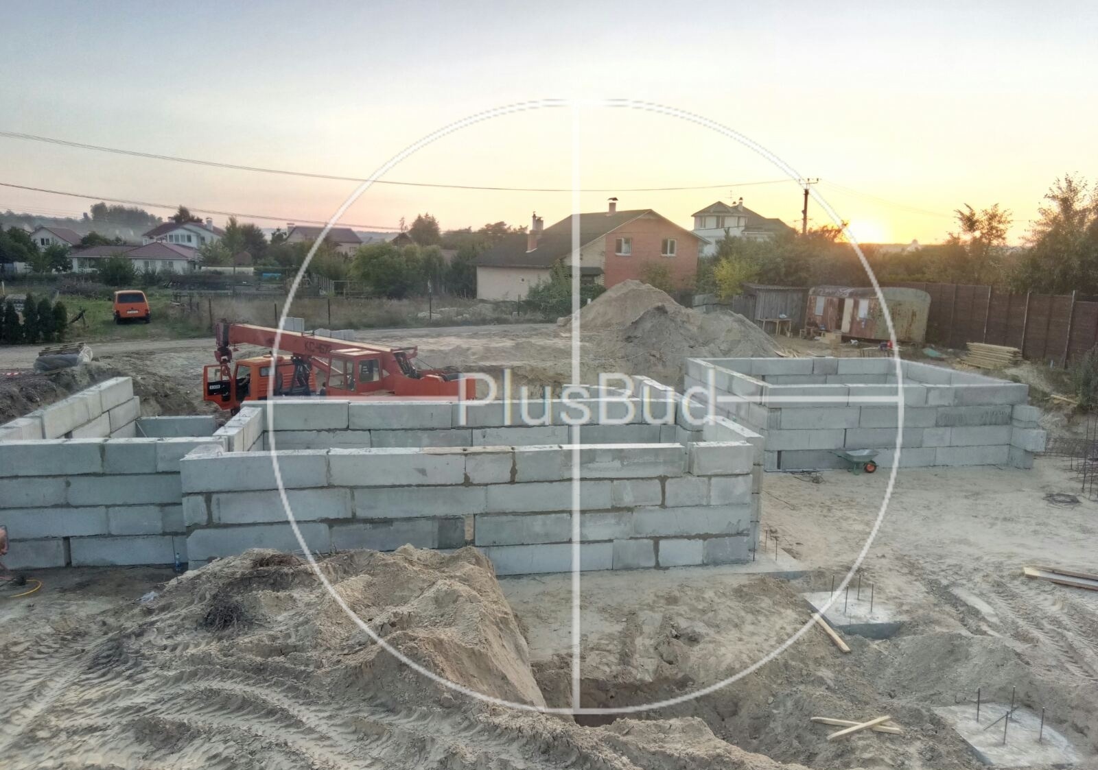 Fundamenty z bloczków betonowych w trakcie budowy domu jednorodzinnego w Warszawie, widoczny żuraw budowlany w tle, ziemia i piasek.