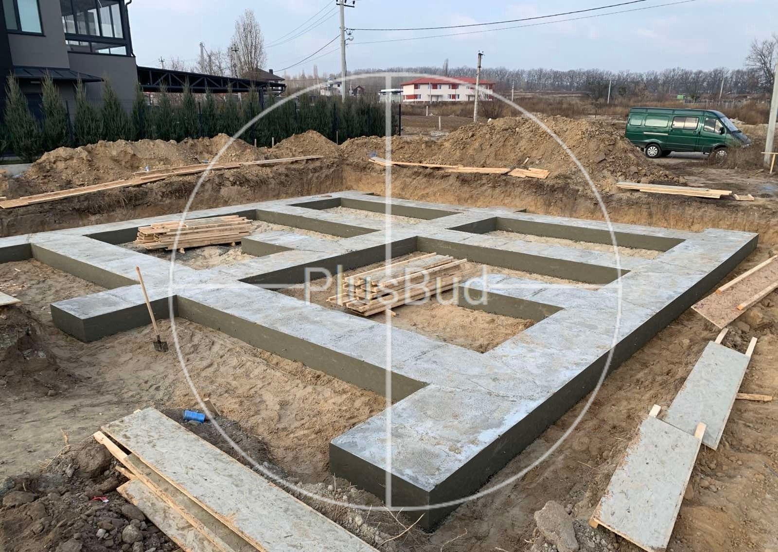 Wylany betonowy fundament domu jednorodzinnego, widoczne deski i wykopana ziemia, zielony bus w tle.