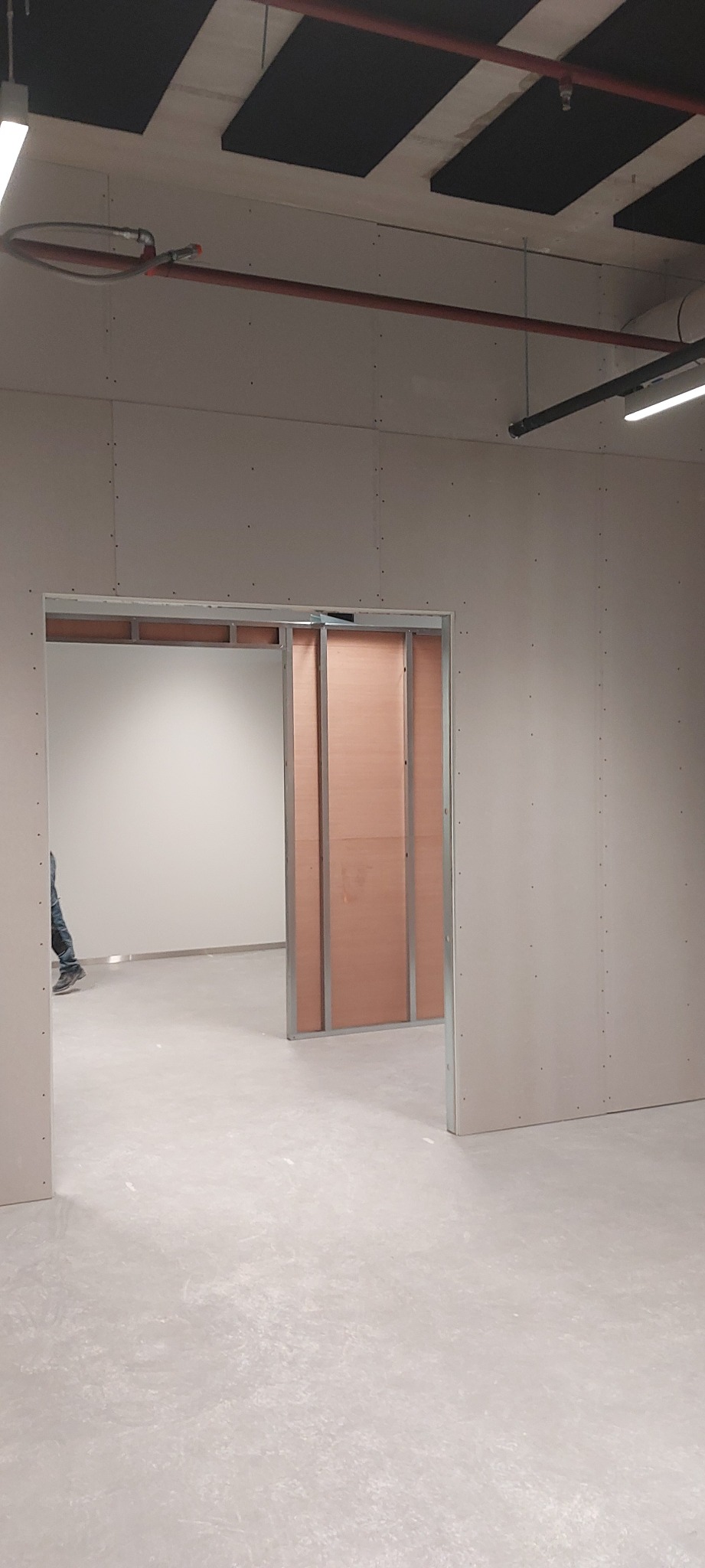 Wnętrze w trakcie prac wykończeniowych, widoczne ściany z płyt, częściowo zabudowane profile, instalacje pod sufitem, betonowa podłoga.