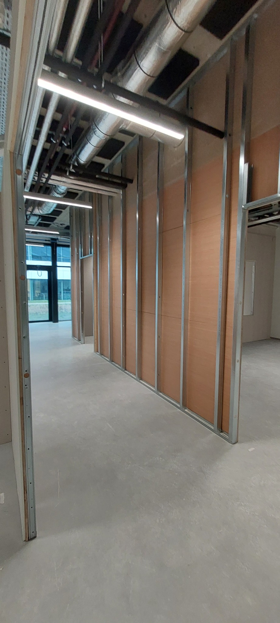 Montaż ścian działowych z płyty kartonowo-gipsowej w biurze, widoczne metalowe profile i fragmenty płyt, sufit z instalacjami.