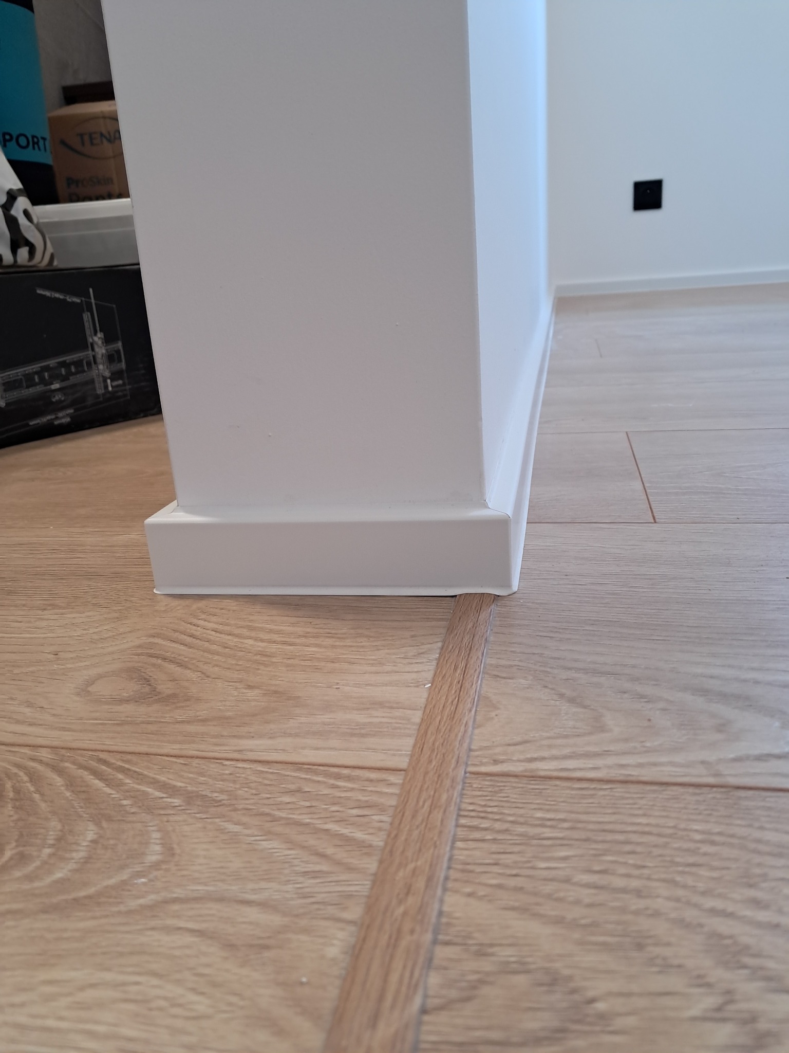 Szczegółowe ujęcie na wykończoną podłogę z paneli, listwę przypodłogową i próg. Widoczna gładka powierzchnia paneli i precyzyjne łączenie elementów.