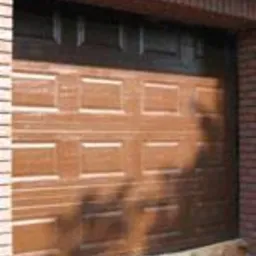 Brązowa, segmentowa brama garażowa z wyraźnymi panelami, oświetlona popołudniowym słońcem, zamontowana w garażu w Dzierżoniowie z ceglanym obramowaniem.