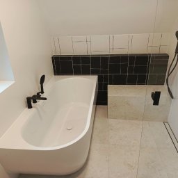 DOM 360 Damian Dobroć - Nowoczesna łazienka z białą wanną, czarną armaturą i mozaiką. Uwagę przykuwa minimalistyczny design i stonowana kolorystyka wnętrza.