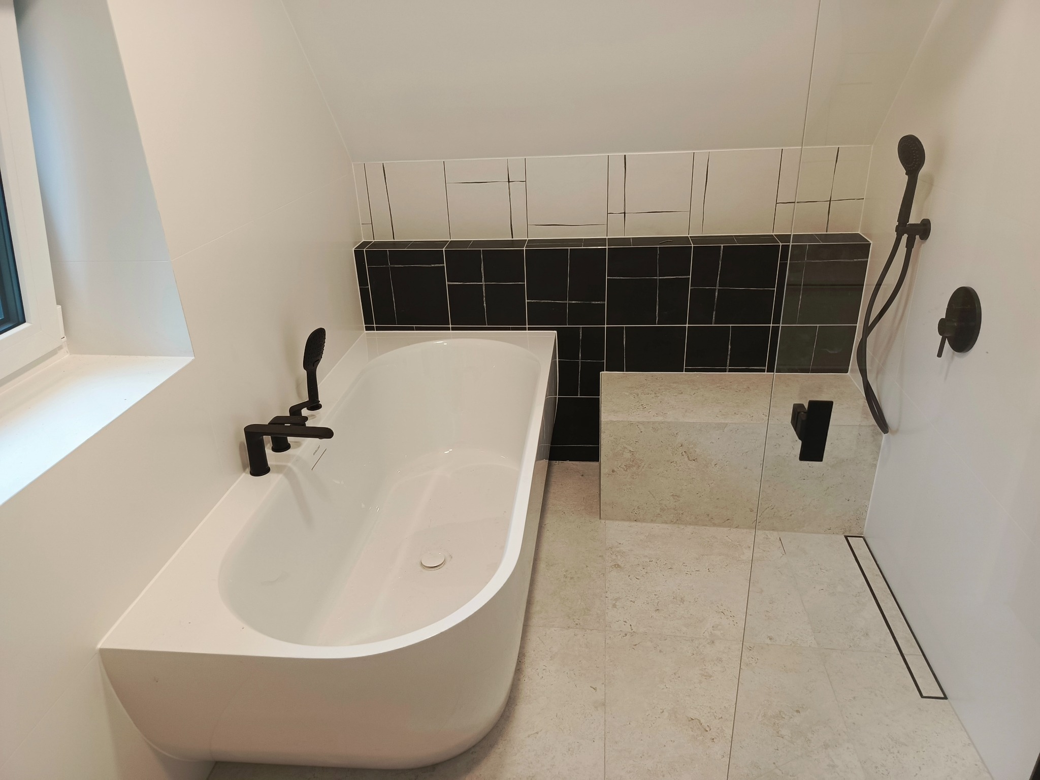 Nowoczesna łazienka z białą wanną, czarną armaturą i mozaiką. Uwagę przykuwa minimalistyczny design i stonowana kolorystyka wnętrza.