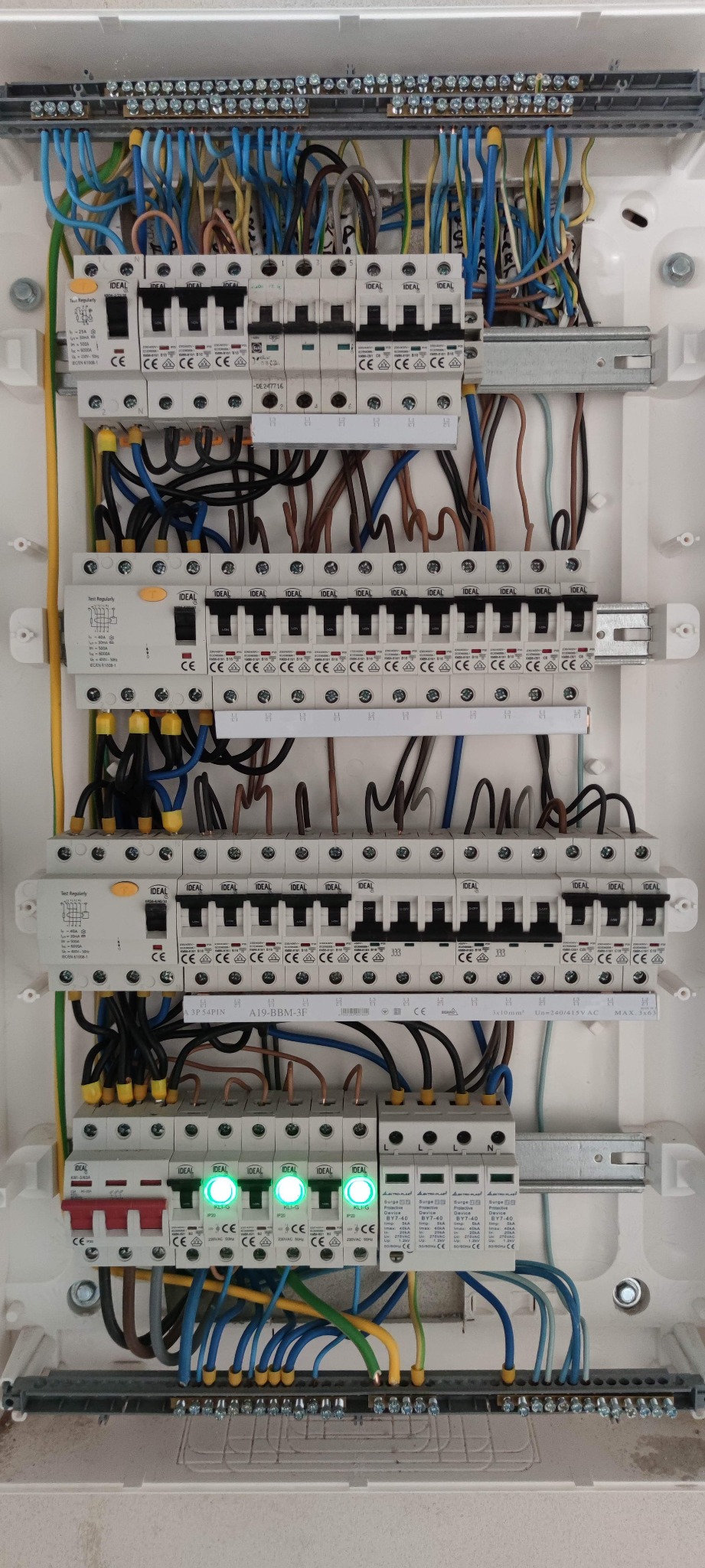 Rozdzielnica elektryczna z zainstalowanymi bezpiecznikami i przewodami, widoczne zielone diody sygnalizujące poprawne działanie, przewody ułożone wewnątrz obudowy.