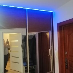 Dan-Mar - Wnętrze przedpokoju z szafą wnękową z przesuwnymi drzwiami lustrzanymi i oświetleniem LED, odbicie osoby robiącej zdjęcie telefonem.