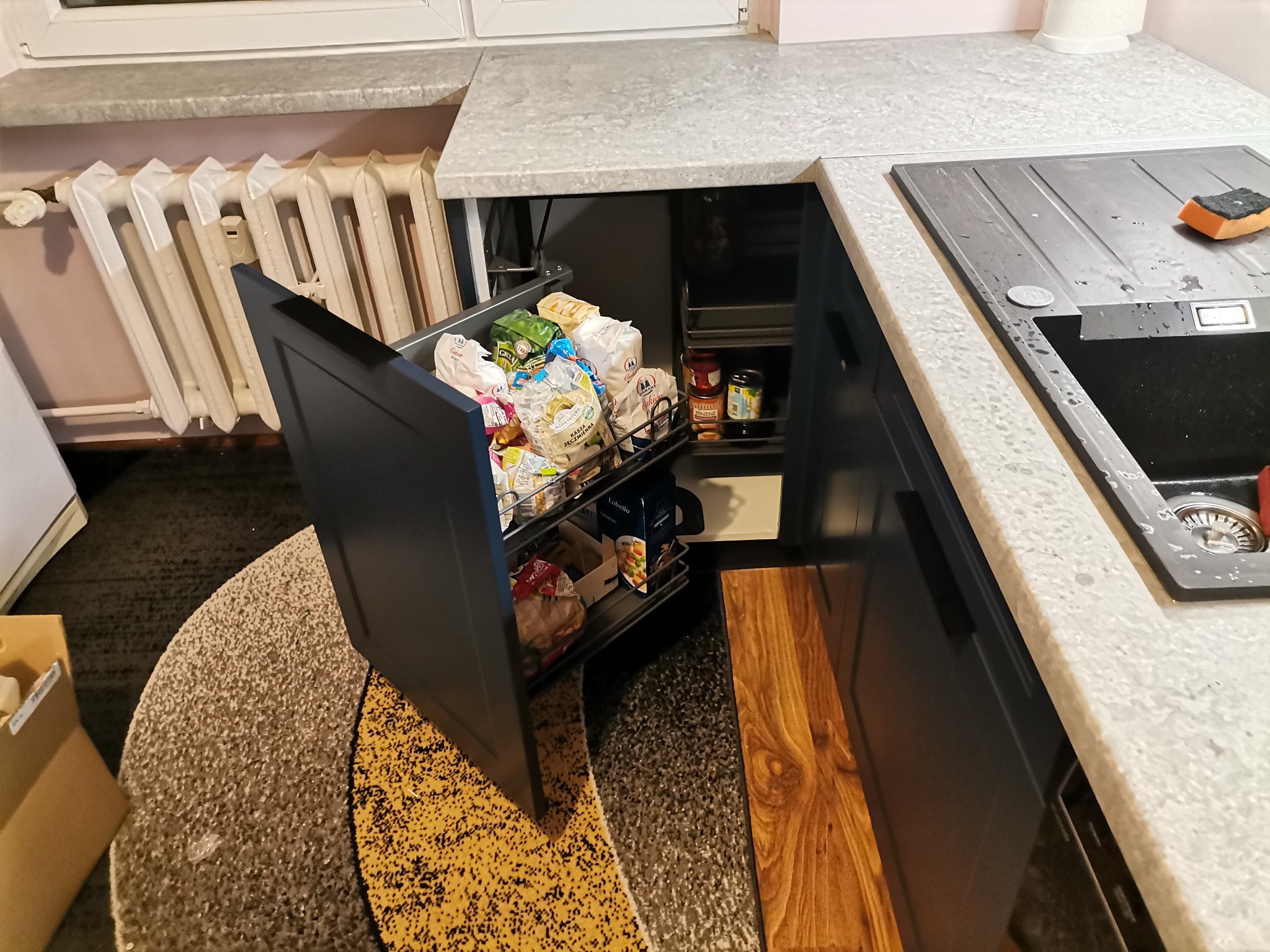 Wysuwana szafka cargo w kolorze granatowym, wypełniona produktami spożywczymi, widoczna obok zlewu i grzejnika.