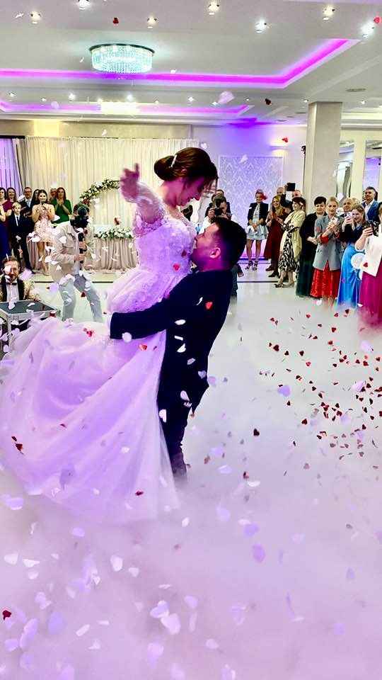 Para młoda w tańcu weselnym, unosząca się w dymie i konfetti, z widocznym zespołem i gośćmi w tle.