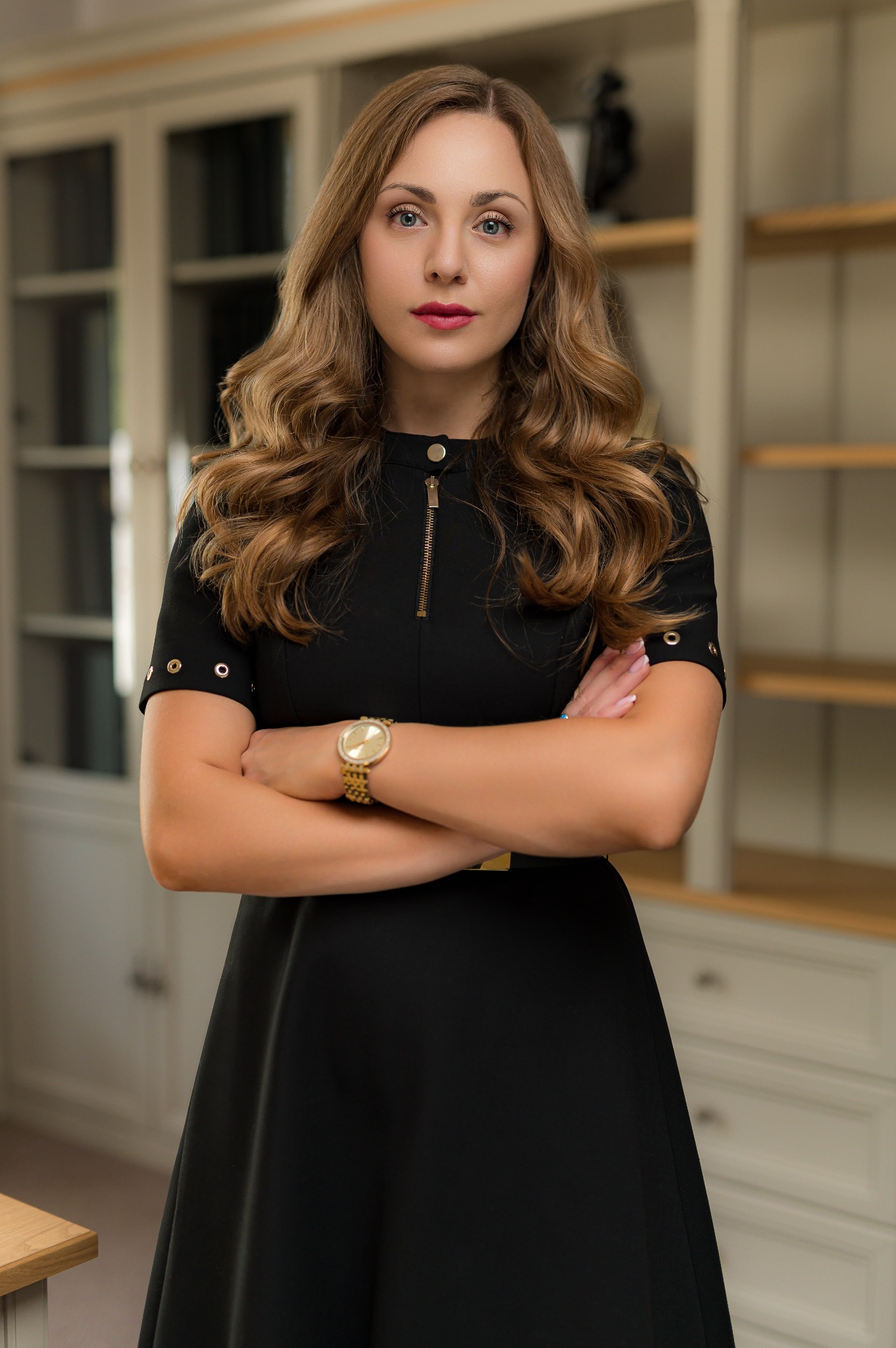 Portret kobiety adwokat w czarnej sukience z rękami skrzyżowanymi na tle regału z książkami w kancelarii